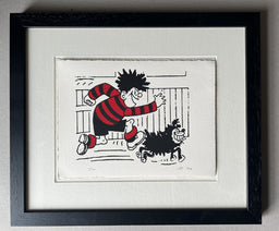 Dennis in his red and black football jersey runs in front of a fence, with gnasher by his side